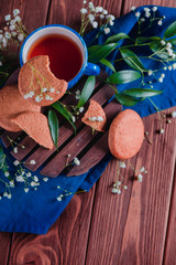 Cup of tea with oatmeal cookies and spring gypsophila flowers on a warm wooden background. Blue ceramic cup on a blue linen napkin. Breakfast scene with copy space.