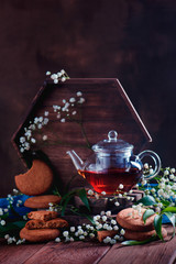 Homemade cookies and a teapot on a warm wooden background with spring gypsophila flowers. Tasty oatmeal pastry with copy space. Country breakfast concept.