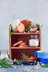 Kitchen shelf with baking ingredients for oatmeal cookies. Flour, milk and sugar on a light background with spring gypsophila flowers and green leaves. Cooking supplies with copy space.