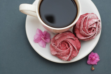 Sweet Pink Meringues and Cup of Coffee on Blue Gray background with Pink Flowers. Spring Background with copy space. Breakfast.