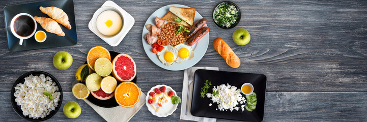Different breakfasts on wooden table. Porridge, curd, fruits, croissants, yogurt, eggs, cottage cheese, apples, english breakfast. Top view, Copy space. Wide panoramic image.