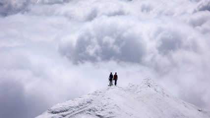 Naklejka na ściany i meble two female mountain climbers on a narrow summit ridge high above cloud banks in the valleys below