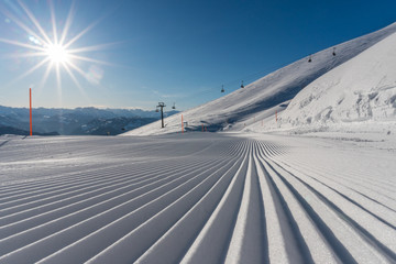 freshly groomed ski slope on a beautiful winter day with sunshine and ski lift in the background