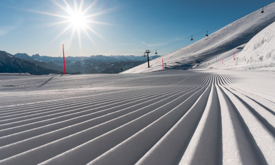 freshly groomed ski slope on a beautiful winter day with sunshine and ski lift in the background