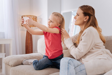 Young photographer. Pleasant cheerful blonde girl smiling and taking a selfie while being together with her mother