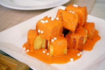 Toast, a piece of square bread baked with butter, topped Thai Milk Tea sauce and decorated with a small piece of white chocolate ball, placed on white dish