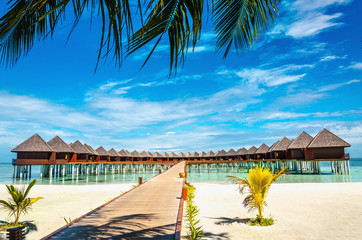 Wooden bridge leading to an exotic bungalow on the background of azure water, maldives