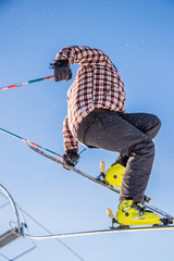 skier with a plaid jacket grabbing the back of his ski while holding poles in the middle of the air close up