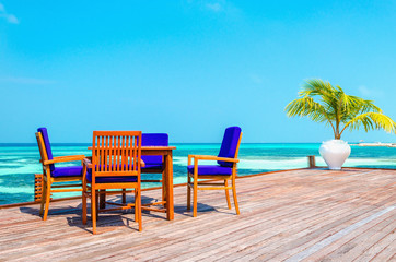 Tables and chairs in a wooden restaurant on stilts on the background of azure water and blue sky