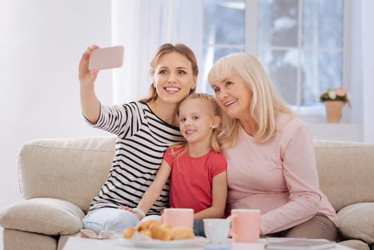 All together. Beautiful nice happy woman holding a smartphone and taking a photo while being with her family
