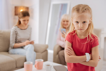 Emotional child. Unhappy cheerless blonde girl sitting on the sofa and turning away from her mother and grandmother while being in a bad mood