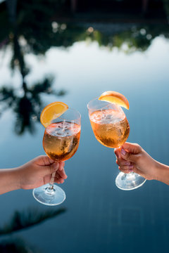 Concept picture of a couple holding glasses of cocktail and cheers by the swiming pool to celebrate their success.