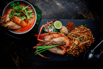 Concept pictures of famouse Thai dishes, Tom Yum Kung & Phad Thai. Beautiful presentation on black stone and black background.
