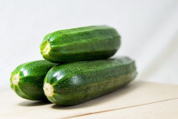 soft focus of three 3 fresh green zucchini on a white background - cocurbita pepo, cocurbitaceae