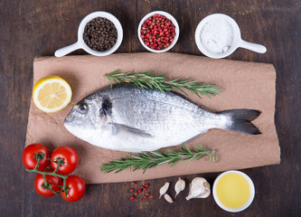 Raw fish dorado cooking and ingredients.  Dorado, lemon, tomato, herbs and spices. Top view on wood table