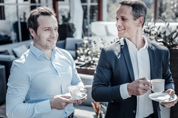 Coffee break. Delighted nice handsome businessmen standing together and enjoying their coffee while having a break from work