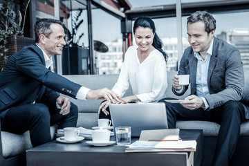 My plan. Nice intelligent happy businessman pointing at the laptop screen and looking at his colleagues while presenting his ideas