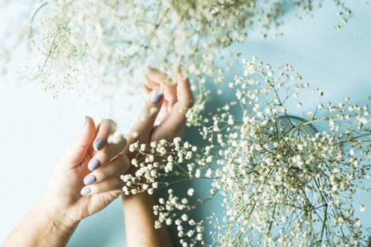 Blue manicure on female nails on a blue background next to the flowers of gypsophila. Trend for gentle pastel colors. Beauty and personal care