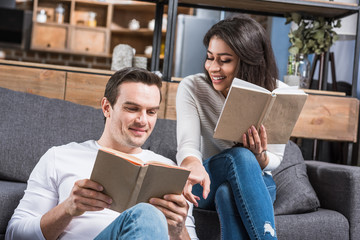 happy multiethnic couple reading books together at home