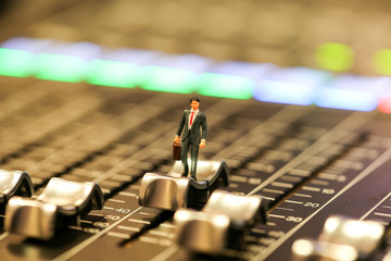 Miniature people : business man standing  on Professional audio mixing console with faders and...