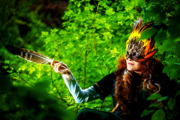 girl with shamanic feather mask and historic dress in woodland surroundings.