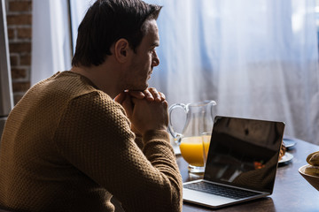 side view of man using laptop with blank screen at home