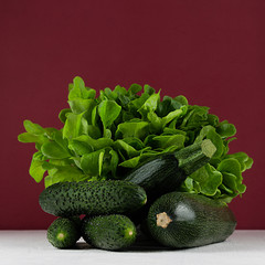 Dark colorful green vegetables on white table and bordo wall. Summer fashion food background.