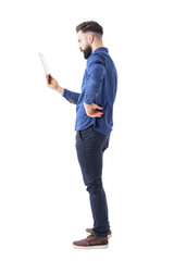 Profile view of serious bearded businessman holding and looking at tablet computer. Full body isolated on white background. 