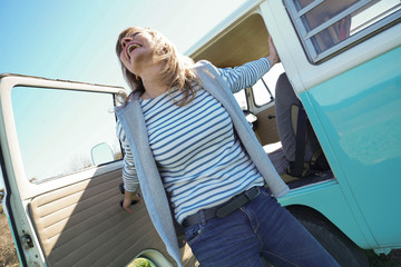 Cheerful mature woman getting off vintage camper van