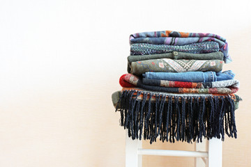 Stack of warm clothes of different patterned fabrics in boho style on a white chair. Empty space.