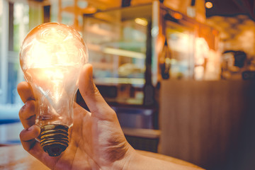 Idea concept with light bulbs in hand and hand of human holding light bulbs on coffee cafe background.