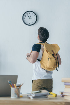back view of male student with backpack looking at clock