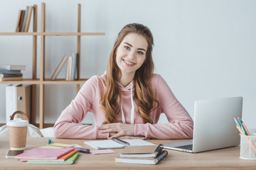 smiling female student sitting at table with laptop and copybooks