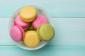multicolored makroon or marshmallows in a plate on green wooden boards
