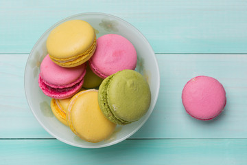 multicolored macarosa in a plate on green wooden boards, macaros lie side by side on boards