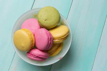 multicolored makroon in a plate on green wooden boards