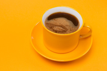 a yellow cup on a yellow saucer, coffee with foam, on a yellow background
