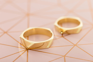Two golden wedding rings on pastel pink background