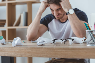 depressed student studying at table with crumpled papers and eyeglasses