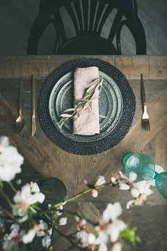 Flat-lay of Spring Easter holiday Table setting. Tender almond blossom flowers, plates, glasses and cutlery over vintage wooden table, top view