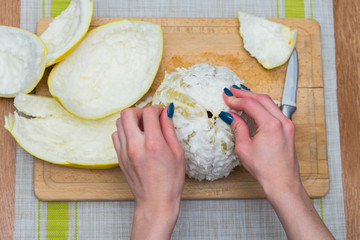 Girl cleans a pomelo on a wooden board