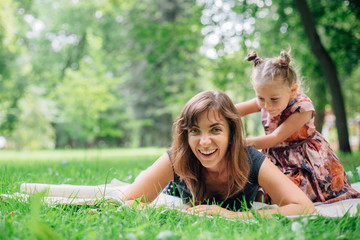 Fototapeta premium Cute little cheerful girl massage her happy mother on grass in park