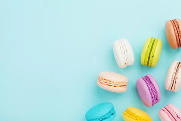Muurstickers Lekkere taart macaron of macaroon op turquoise pastel achtergrond van bovenaf. Kleurrijke Franse koekjes op dessert bovenaanzicht. © juliasudnitskaya