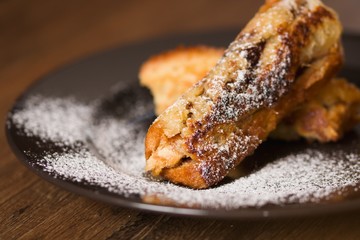 Detail of rolled french toast on black plate and covered by powdered sugar