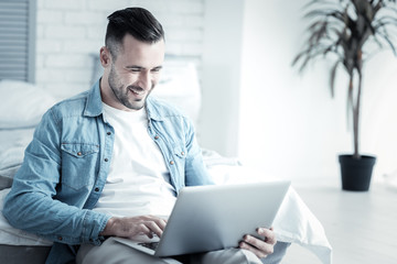 Favourite job. Cheerful nice positive man looking at the laptop screen and smiling while working on it