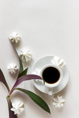Creative layout. Coffee in a white cup on a saucer on a white background. Green flower leaves. meringue. Place for text. Flat lay