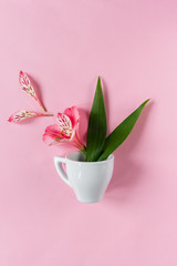 A small white cup of coffee with bright flowers on a pink background. The concept. Creative layout. Place for text. Flat lay