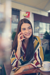 Smiling young woman talking on phone at cafe.