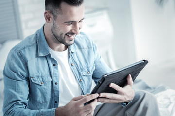 Naklejka na ściany i meble Modern technology. Delighted positive handsome man holding a tablet and smiling while using it