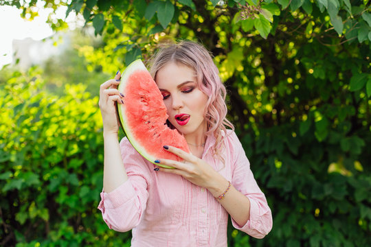 Beautiful young woman with pink hair enjoying watermelon